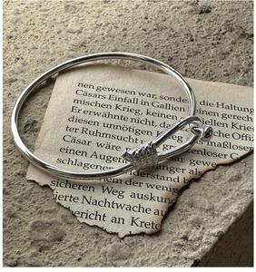 Detailed view of silver knot bangle with nautical hook on vintage paper background