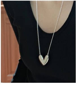 Close-up of a hollow S925 sterling silver heart pendant on a delicate chain over a black top