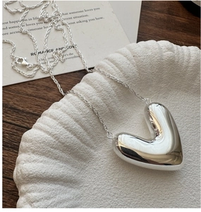 Close-up of a polished silver heart pendant necklace on a minimalist ceramic plate