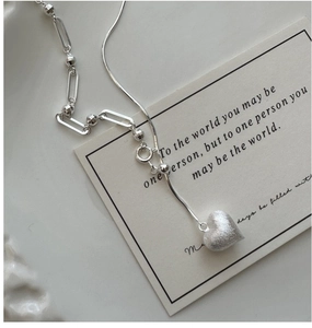 Detail of S925 sterling silver heart necklace featuring a matte brushed texture and asymmetric chain