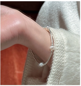 Close-up of minimalist S925 silver tube and pearl bracelet on a knit sweater sleeve