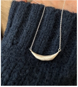 Close-up of a brushed S925 sterling silver smile pendant necklace on blue sweater