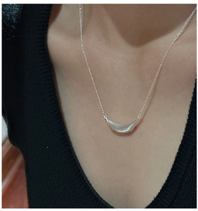 Close-up of minimalist silver curved pendant with textured surface on collarbone chain