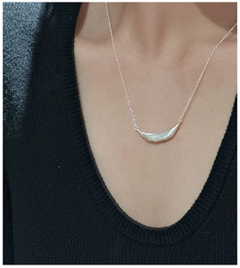 Macro shot of a brushed S925 sterling silver smile pendant on a dainty chain over black knit