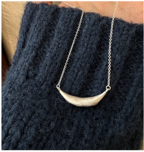 Close-up of minimalist brushed silver smile pendant necklace worn on a dark sweater