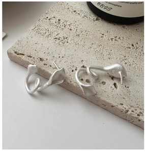Macro view of matte S925 sterling silver petal earrings on textured beige stone