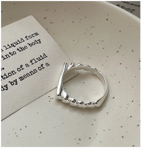 Detail shot of a liquid-form S925 silver heart ring on a textured ceramic dish