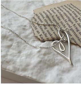 Macro detail of silver S925 heart knot pendant necklace with delicate ball chain on stone