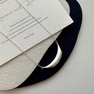 Minimalist S925 sterling silver smile necklace with brushed texture on a poetic paper background
