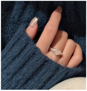 Detail of matte S925 sterling silver heart ring worn on hand with blue knit sweater background