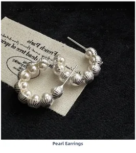 Detail of C-shaped silver earrings with white pearls on a dark textured surface