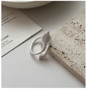 Macro shot of matte silver leaf ring resting on textured stone with minimalist backdrop