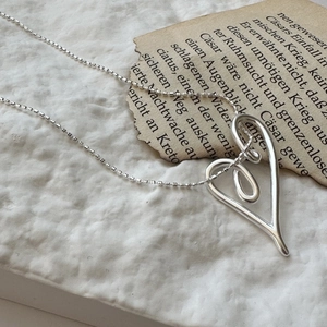 Minimalist S925 sterling silver heart knot necklace on a vintage paper background