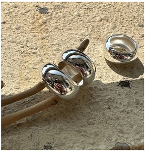Three minimalist polished silver rings displayed on natural wood and sand stone