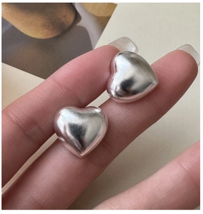 Detail macro view of matte S925 sterling silver hollow heart earrings held by hand
