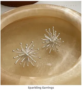 Macro shot of silver fireworks stud earrings with radial design on marble texture