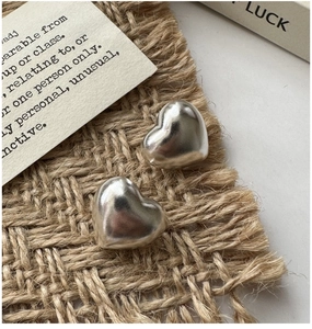 Macro shot of polished S925 sterling silver heart-shaped stud earrings on linen base