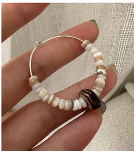 Detail view of a handmade S925 silver hoop earring with white shell beads and wood accents