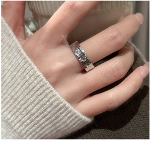 Close-up of a hammered silver ring on a finger with a cozy white knit sweater background
