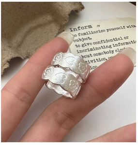 Macro shot of matte silver rings with engraved heart and flower patterns worn on a finger