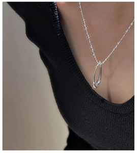 Detail of a silver oval pendant with a beaded chain on a black knit background