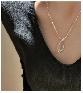 Close-up of minimalist S925 sterling silver oval pendant on delicate beaded chain