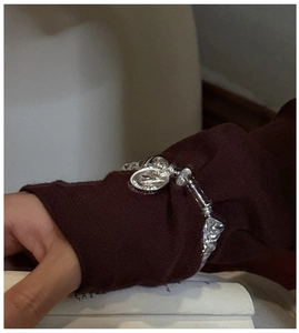 Macro view of S925 silver beaded bracelet with bird pendant on a vintage knit sleeve
