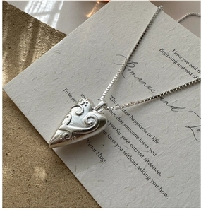 Macro view of vintage heart pendant with floral engraving on a delicate silver box chain