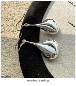 Macro shot of silver teardrop earrings with polished finish on black velvet and stone textures
