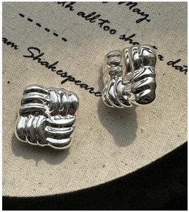 Macro detail of S925 sterling silver square knot stud earrings on a textured cloth