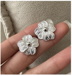 Detail of silver S925 floral stud earrings featuring textured petals and a mirror core