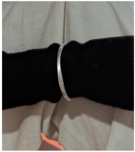 Close-up of minimalist brushed S925 sterling silver bangle on a female wrist over black fabric