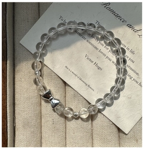 Detail of silver bow charm and clear crystal beads on a textured jewelry tray