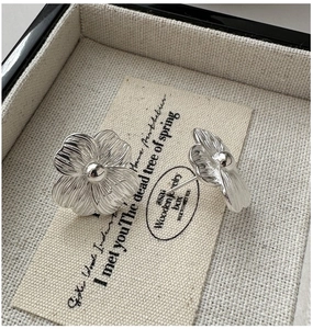 Close-up of S925 sterling silver flower stud earrings with brushed texture on linen card