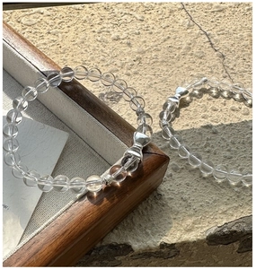 Detailed close-up of white crystal beaded bracelets with silver bow charm on stone background