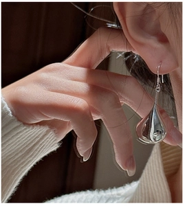 Close-up of silver hollow teardrop earrings with mirror finish worn by a model