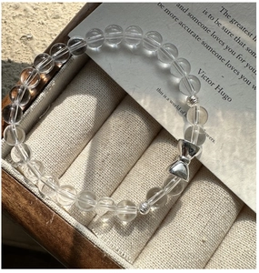 Detail of beaded bracelet with silver bow charm and white crystals in a beige jewelry box