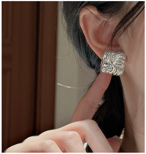 Detailed view of silver square stud earrings with textured finish worn on ear