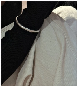 Close-up of minimalist silver bangle styled over a black knit sleeve for a modern look