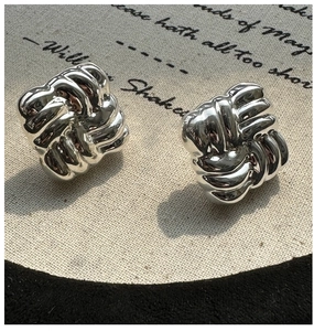 Macro shot of silver woven knot earrings on a textured fabric background