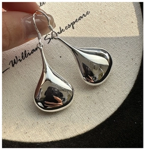 Macro shot of silver teardrop earrings with a mirror polished finish on burlap