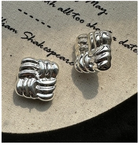 Close-up of S925 silver stud earrings with square woven texture on vintage burlap