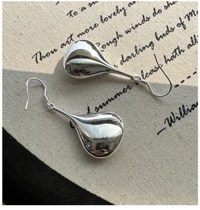 Macro detail of polished sterling silver teardrop earrings on minimalist linen background