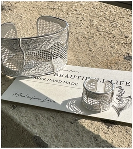 Macro view of textured grid S925 silver ring and cuff bracelet set on stone surface