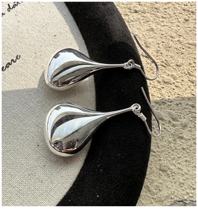 Macro shot of silver teardrop earrings with a polished surface on a beige canvas background