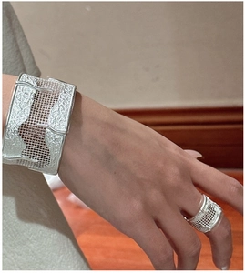 Macro detail of textured grid silver bangle and ring with fluid relief pattern