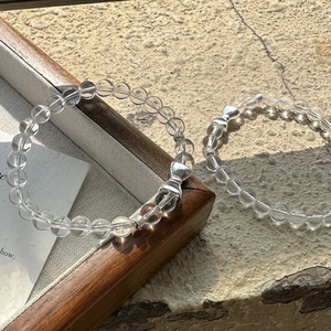 S925 silver bow bracelet with transparent white crystals on a rustic textured background