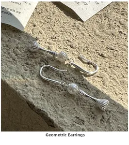 Minimalist silver geometric dangle earrings with a single pearl on a stone surface