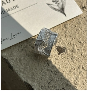 Detailed close-up of wide S925 silver ring with woven texture on a stone surface