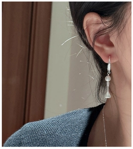 Detailed view of silver hoop earrings with white pearl and textured umbrella pendant on model